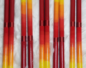 May include: Ten cylindrical wooden sticks arranged in pairs, each featuring a vertical color gradient transitioning from deep red at the top to bright yellow at the bottom, with two distinct bands of metallic red thread wrapped around the center.