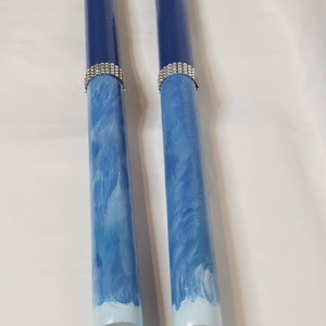 May include: Two cylindrical wooden rods featuring a dark blue top section, a silver-toned rhinestone band, and a light blue base with white brushstroke patterns. The rods have a smooth finish and are positioned vertically side by side.