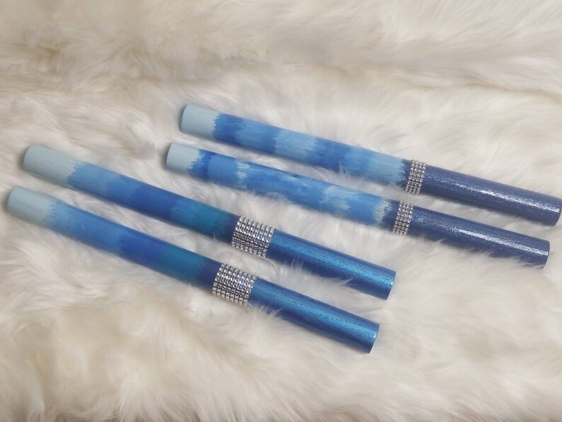 May include: Four cylindrical pens featuring a blue ombre gradient finish that transitions from light to dark blue. Each pen is accented with a band of silver-toned rhinestones positioned near the darker end of the barrel, creating a decorative detail.