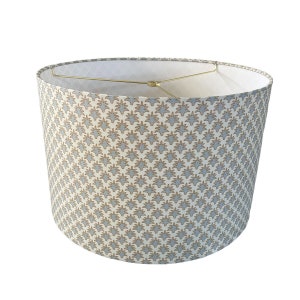 May include: A white lampshade with a blue and brown geometric pattern. The lampshade is round and has a gold metal frame.