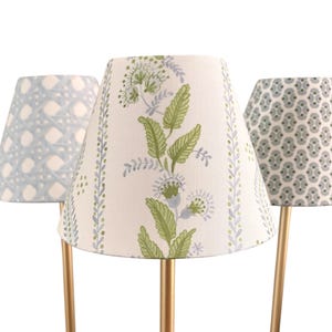 Puede incluir: Tres lámparas decorativas con bases doradas y pantallas estampadas. Las pantallas presentan diseños en azul, verde y blanco. Los patrones incluyen un enrejado, floral y geométrico. Las lámparas están sobre un fondo blanco.