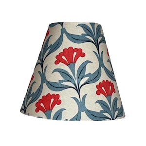 May include: A cone-shaped lampshade with a floral pattern. The lampshade is white with blue and red floral designs. The flowers are red with a blue center and the leaves are blue.