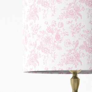 May include: A white lampshade with a pink floral pattern. The lampshade is made of fabric and has a smooth finish.