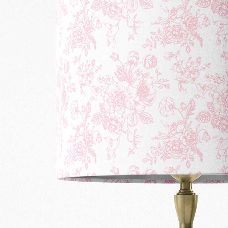 May include: A white lampshade with a pink floral pattern. The lampshade is made of fabric and has a smooth finish.