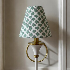 May include: A white and gold lamp with a green and white patterned lampshade. The lampshade has a repeating leaf design. The lamp has a circular gold accent and a white base.