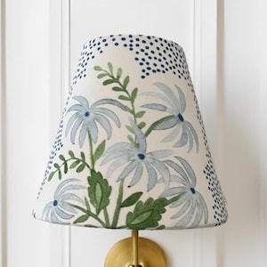 K&ouml;nnte beinhalten: Ein wei&szlig;er Lampenschirm mit einem blauen und gr&uuml;nen Blumenmuster. Der Schirm hat eine konische Form und ist aus Stoff.