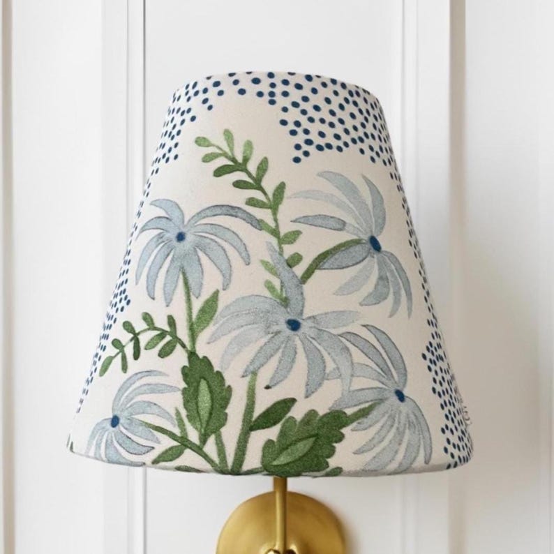 K&ouml;nnte beinhalten: Ein wei&szlig;er Lampenschirm mit einem blauen und gr&uuml;nen Blumenmuster. Der Schirm hat eine konische Form und ist aus Stoff.