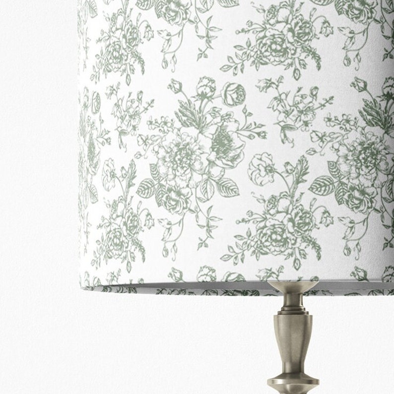 May include: A white lampshade with a green floral pattern. The lampshade is on a silver lamp base.