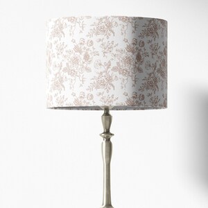 May include: A silver table lamp with a white lampshade featuring a delicate floral pattern in a light brown color.