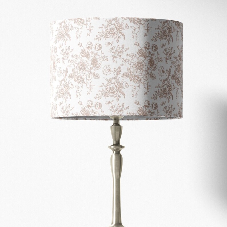 May include: A silver table lamp with a white lampshade featuring a delicate floral pattern in a light brown color.