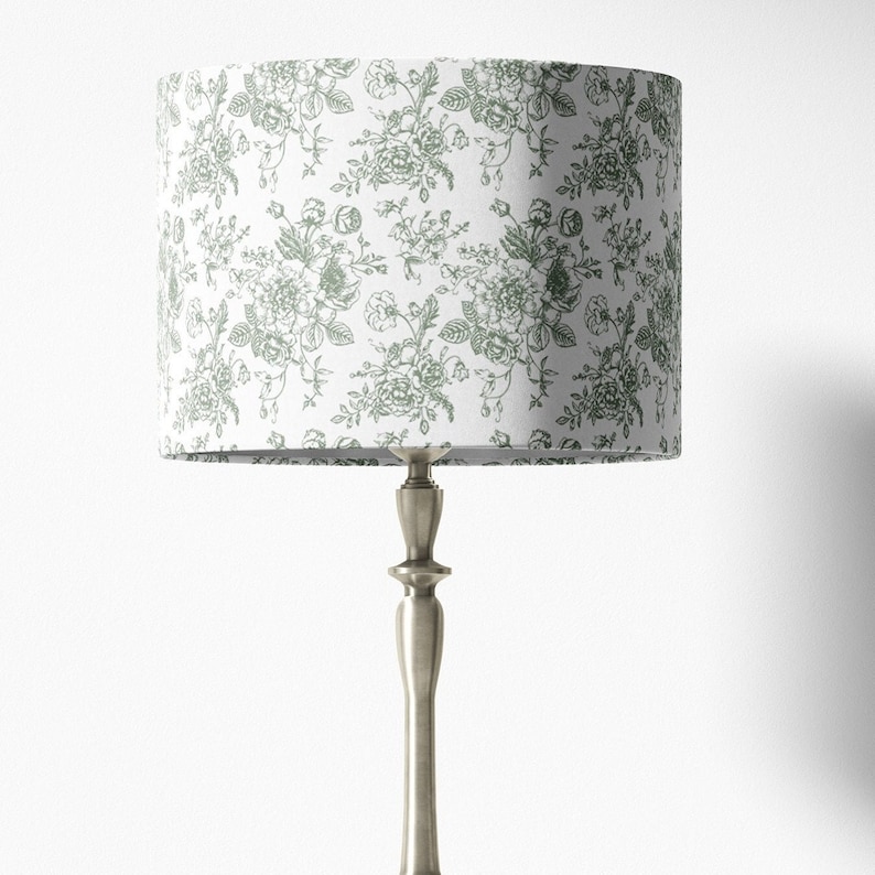 May include: A silver table lamp with a white lampshade featuring a green floral pattern.