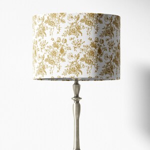May include: A white lampshade with a gold floral pattern. The lampshade is on a silver lamp base.