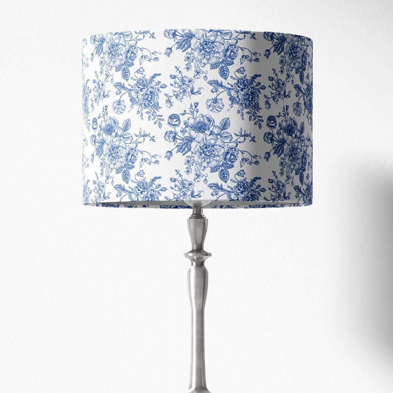 May include: A silver table lamp with a white lampshade featuring a blue floral pattern.
