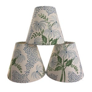 May include: Three cream-coloured lampshades with a floral pattern. The design features light blue flowers and green leaves, with a border of small blue dots. The shades are stacked, showcasing the pattern.