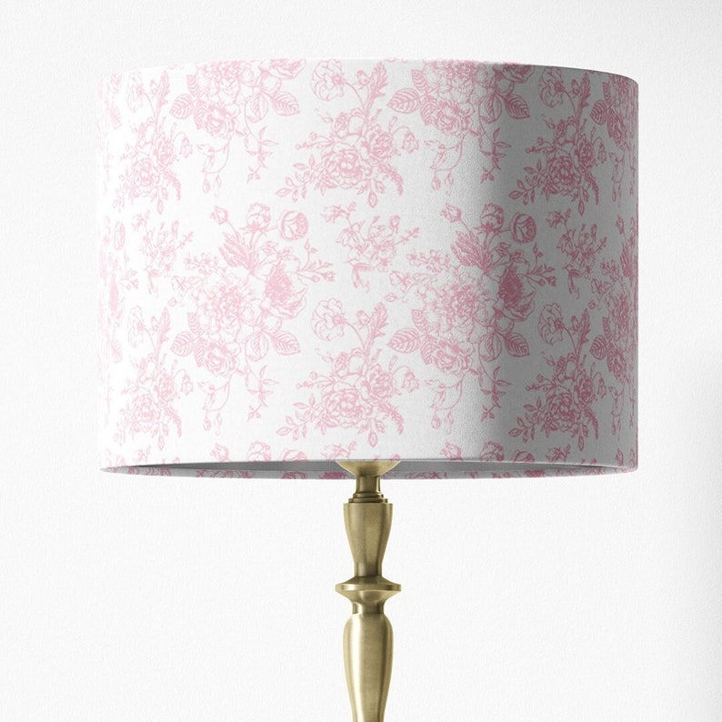 May include: A white lampshade with a pink floral pattern. The lampshade is on a gold lamp base.