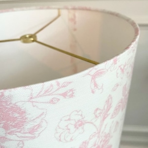 May include: A white lampshade with a pink floral pattern. The lampshade is made of fabric and has a gold metal frame.