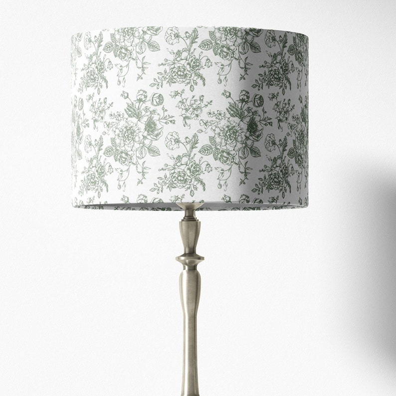 May include: A white lampshade with a green floral pattern. The lampshade is on a silver lamp base.