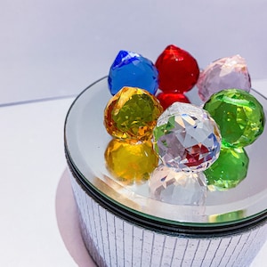 Può includere: Una scatola a specchio argentata con un coperchio che contiene sei sfere di cristallo sfaccettate di vari colori: rosso, blu, verde, giallo, rosa e trasparente.
