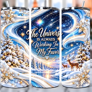 Puede incluir: Un vaso cilíndrico de acero inoxidable con un paisaje invernal de pinos nevados, un ciervo y una luna creciente. El diseño incluye copos de nieve dorados y el texto, The Universe IS ALWAYS Working In My Favor.