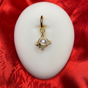 May include: Gold hoop earring with a pearl and green airplane charm. The charm is attached to a small gold ring.