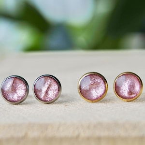 Könnte beinhalten: Vier Ohrstecker mit pinkfarbenem Glitzer-Finish. Zwei Ohrstecker haben eine silberne Fassung und zwei Ohrstecker haben eine goldene Fassung.