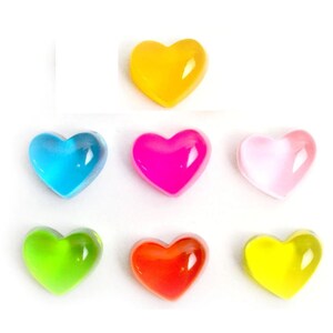 May include: Seven heart-shaped, translucent decorative embellishments in various colors: yellow, blue, pink, light pink, green, red-orange, and light yellow. These small, glossy hearts are arranged on a white background.
