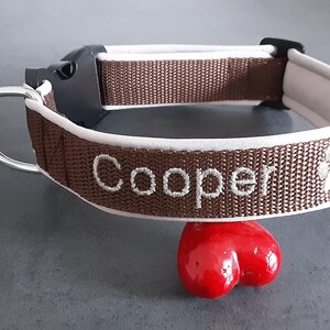 May include: Brown dog collar with white trim and the name "Cooper" embroidered in white. A paw print is also embroidered on the collar.