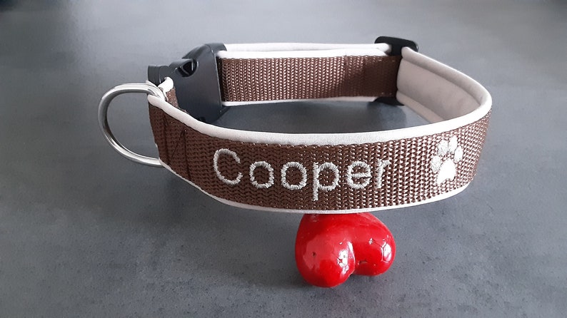 May include: Brown dog collar with white trim and the name "Cooper" embroidered in white. A paw print is also embroidered on the collar.