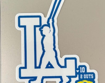 May include: A blue and white sticker featuring the letter "L" with a baseball player silhouette. The sticker also includes the text "10 2 OUTS" in a yellow and blue box, likely representing a baseball team.