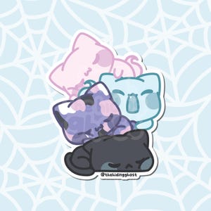 May include: A sticker featuring four cartoon cat faces in various colors: pink, blue, purple, and black. The purple cat has a spotted pattern. The sticker has a white border and the text "@thehidingghost" at the bottom.