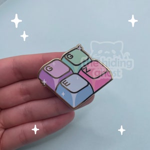 May include: A colorful enamel pin shaped like four keyboard keys. The keys are arranged in a square shape and feature the letters 'G', 'E', 'Z', and 'N'. The pin has a gold outline and a sparkly finish.