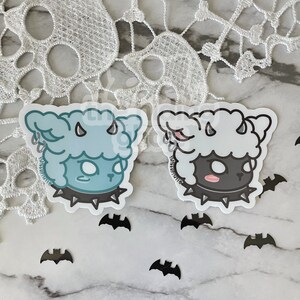 May include: Two black and white cartoon sheep stickers with horns and studded collars. The sheep are on a white marble surface with black bats scattered around them.