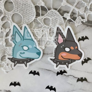 May include: Two sticker designs of dogs with punk rock accessories. The dog on the left is light blue with a silver nose ring and a studded collar. The dog on the right is black and brown with a silver nose ring and a studded collar. Both dogs have a white eye and a pink cheek.