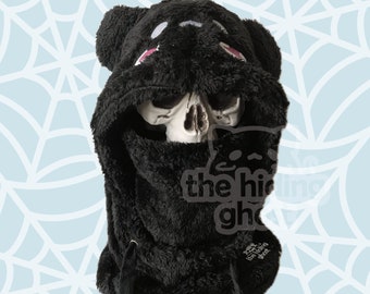 Puede incluir: Fleece negro con capucha con cara de oso y detalles en rosa. La capucha está subida y cubre la cara. El texto "the hiding ghost" es visible en la parte delantera de la capucha.