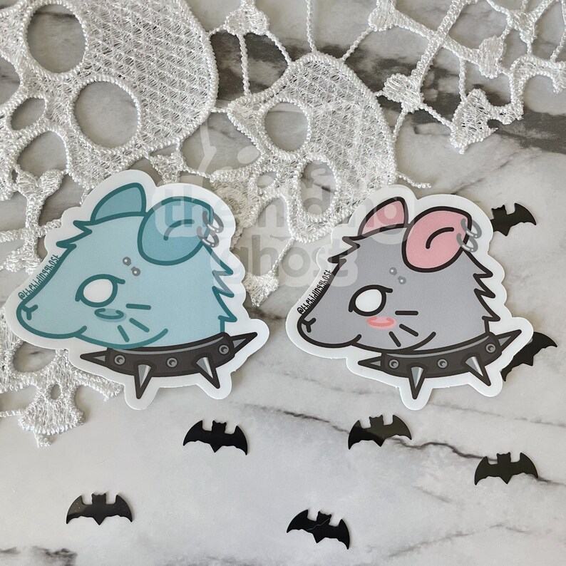May include: Two cartoon rat stickers with punk rock accessories. The rat on the left is light blue with a black studded collar. The rat on the right is grey with a pink ear and a black studded collar. Both rats have black eyes and white pupils. The stickers are on a white background with black bats.