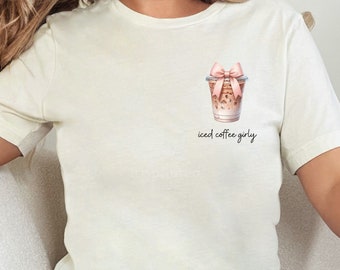 May include: A white t-shirt with a graphic of a cup of iced coffee with a pink bow on top. The text "iced coffee girly" is printed below the cup.