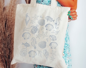 May include: A white canvas tote bag with a blue and white design of seashells, starfish, seahorses, and a fish. The bag has two handles.