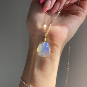 May include: A gold chain necklace featuring a large, pale blue stone pendant, encased in gold wire. A delicate silver bracelet is also visible. The necklace is a stylish accessory.