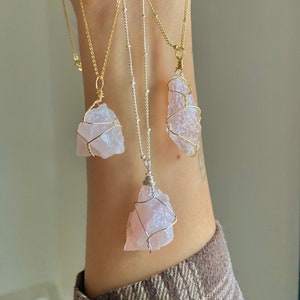 May include: Three necklaces with rose quartz pendants wrapped in gold wire. The necklaces are on a model's arm and have different chain styles.