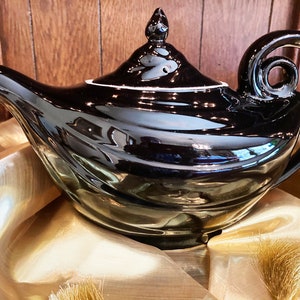 May include: A black ceramic teapot with a genie lamp design. The teapot has a shiny, glossy finish and a white rim around the lid.