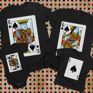 May include: A collection of black garments featuring playing card designs. One t-shirt displays a King of Spades, another a Queen of Spades, a third a smaller t-shirt with an Ace of Spades, and a black baby bodysuit featuring a Jack of Spades.