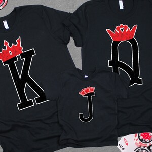 May include: Three black t-shirts with a red and white playing card design. The shirts feature a King, Queen, and Jack of Hearts.