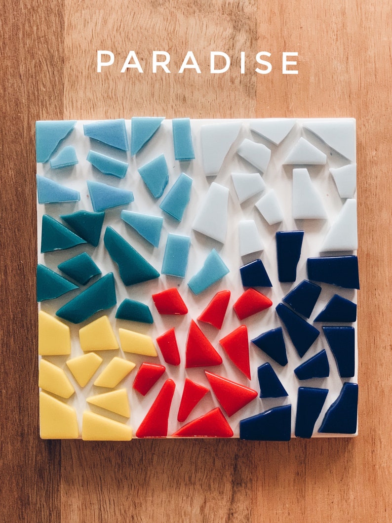 Puede incluir: Un posavasos cuadrado de mosaico con fondo blanco y cuatro secciones de piezas de vidrio de diferentes colores. Las secciones son azules, verde azulado, rojas y azul oscuro.