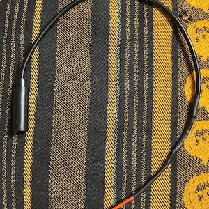 Peut inclure: Un câble électronique noir doté d'un connecteur cylindrique à une extrémité et d'un petit connecteur en plastique blanc à deux broches à l'autre. Le câble est fin et flexible, avec une courte section de fils rouge et noir près du connecteur.