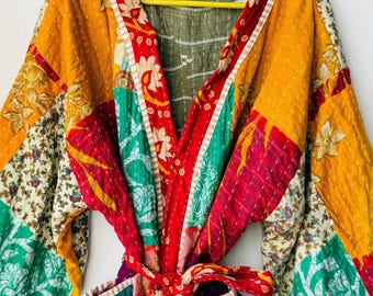 May include: A patchwork robe with a vibrant mix of colors, including yellow, red, green, and teal. The robe features floral and geometric patterns, with a red tie belt. The garment is hanging on a yellow hanger.