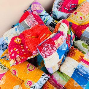 May include: A pile of colorful, patchwork quilts. The quilts feature a variety of patterns and colors, including red, yellow, blue, and green. The quilts appear to be made of cotton and have a quilted texture.