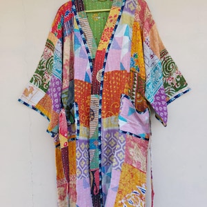 Könnte beinhalten: Ein bunter Patchwork-Kimono mit V-Ausschnitt und langen Ärmeln. Das Kleidungsstück besteht aus verschiedenen Stoffquadraten, die zusammengenäht sind und rosa, gelbe, orange und violette Farbtöne aufweisen. Das Design des Kimonos ist einzigartig und farbenfroh.