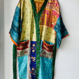 May include: A patchwork kimono robe with a vibrant mix of colors and patterns. The robe features a green collar and trim, with patches of teal, yellow, and pink fabrics. It has a tie belt and two pockets.