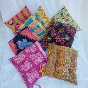 May include: A set of six colourful, square, quilted floor cushions. The cushions are made from a variety of fabrics, including floral prints, paisley patterns, and geometric designs. The cushions are all tied with colourful ribbons.