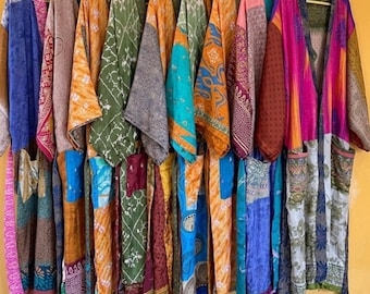 May include: A collection of colorful, patterned kimonos hanging on a clothing rack. The kimonos feature various designs in shades of blue, orange, green, and pink. The background is a solid yellow wall.